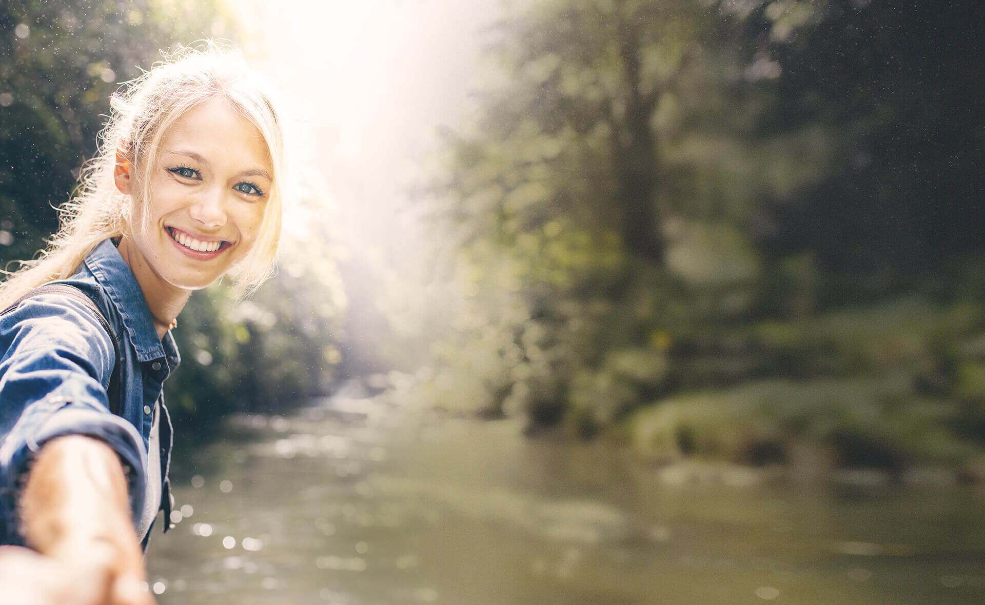 Hakawerk Header: junge Frau vor Fluss am linken Bildrand, in die Kamera lächelnd